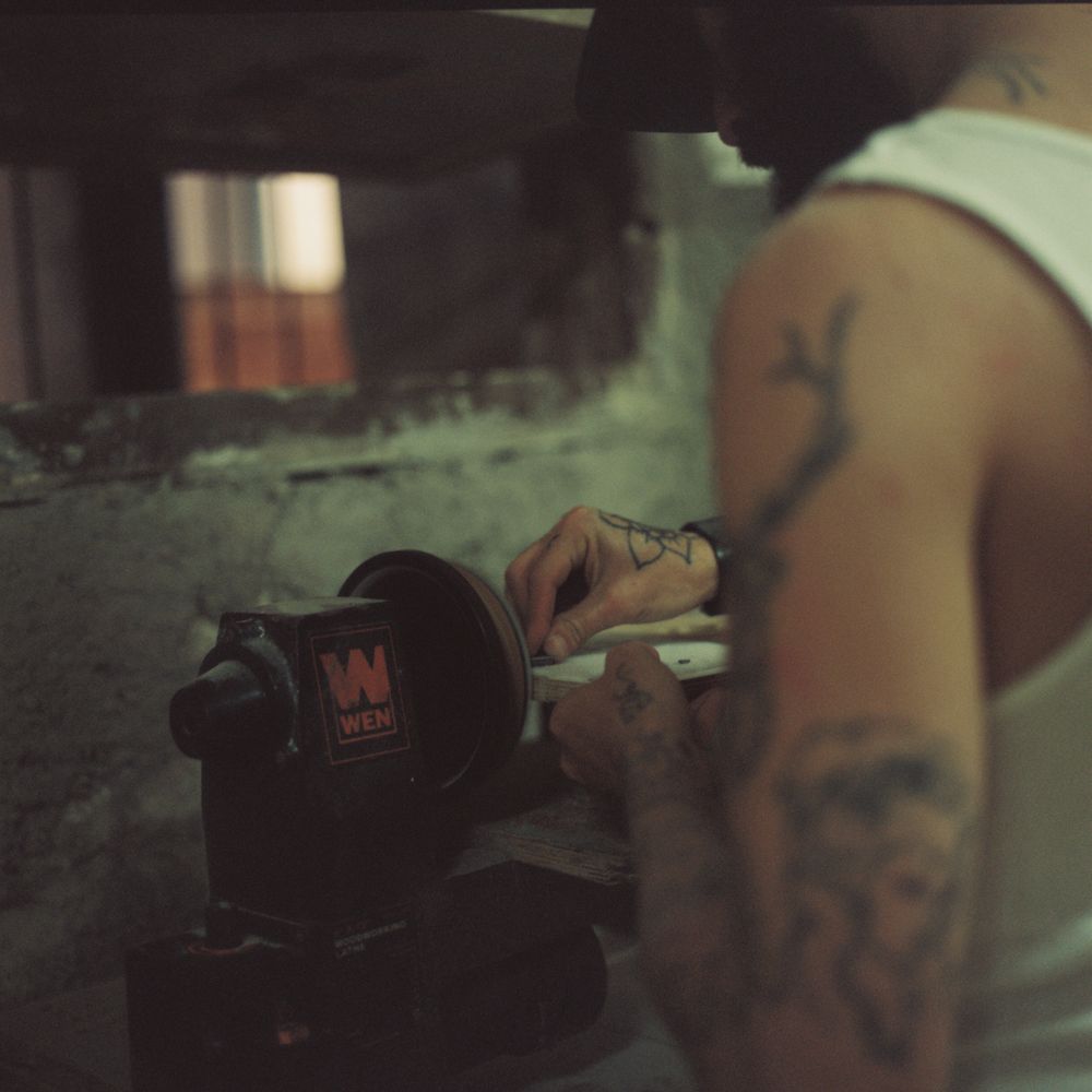 Tattooed hands shaping a board at the grinder